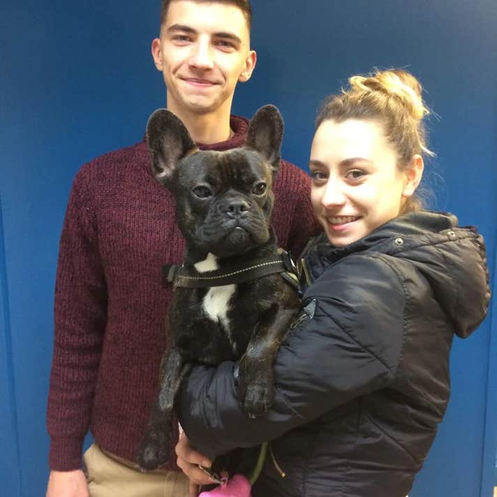 Un chico y una chica  con un perro buldog francés negro en brazos en la clínica veterinaria El Jardín.